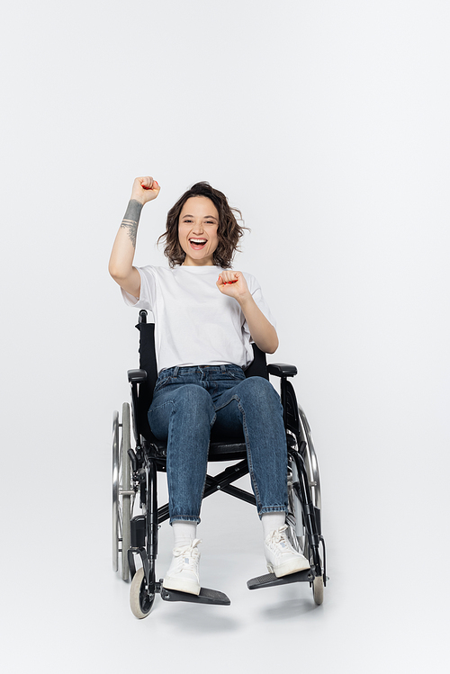 Excited woman in wheelchair showing yes gesture on grey background