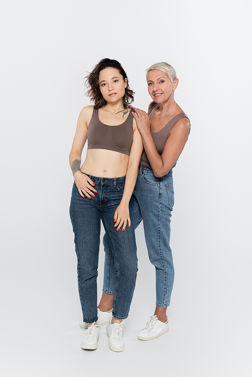 Full length of smiling senior woman hugging friend on grey background