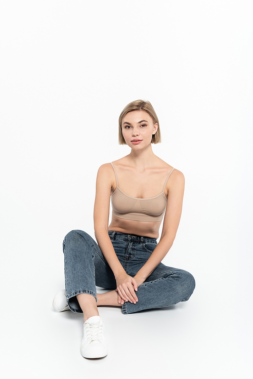 Blonde woman in top and jeans sitting on grey background