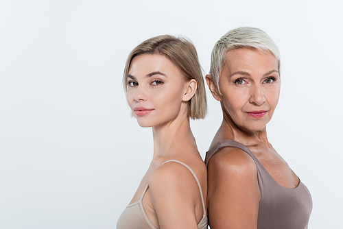 Women looking at camera while standing back to back isolated on grey