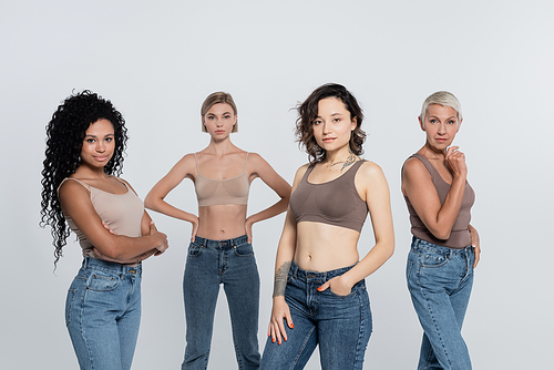 Brunette woman in top posing near interracial friends isolated on grey, feminism concept