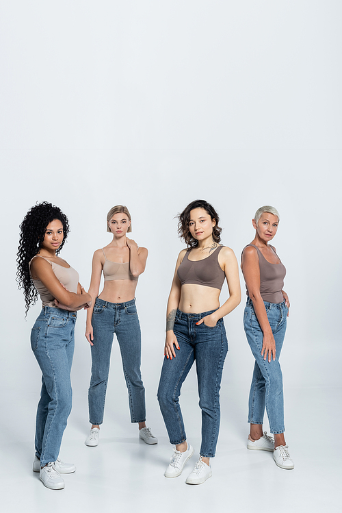 Full length of multiethnic friends in jeans and tops posing on grey background