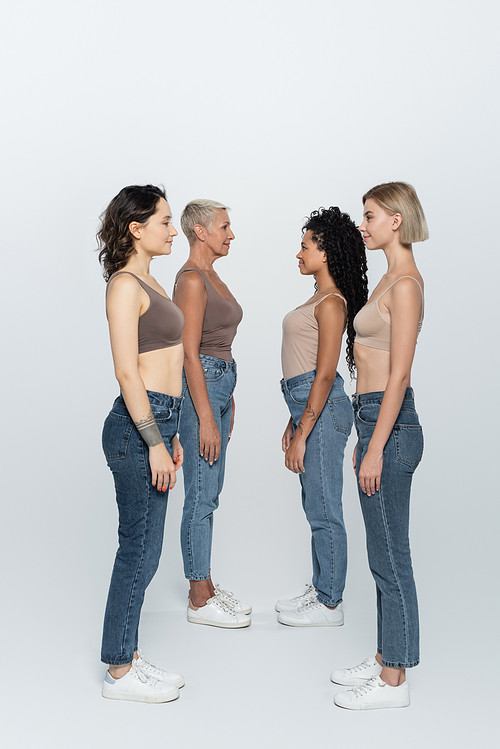 Side view of interracial women looking at each other on grey background