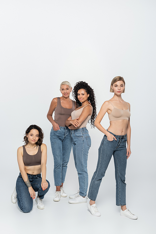 Young women posing near interracial friends on grey background