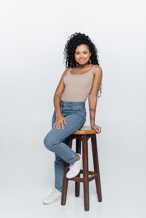 Happy african american woman posing near chair on grey background