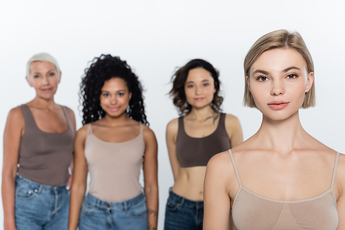 Blonde woman looking at camera near blurred interracial friends isolated on grey