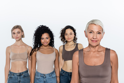 Senior woman looking at camera near blurred interracial friends isolated on grey