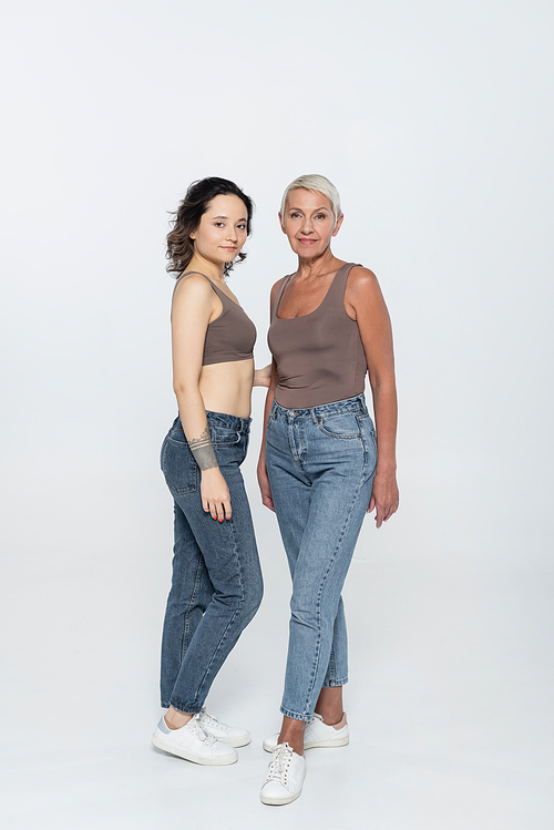 Full length of smiling women posing and looking at camera on grey background