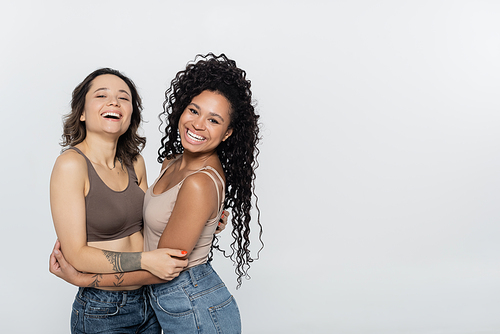 Curly african american woman hugging cheerful friend isolated on grey, feminism concept