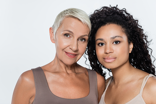 Curly african american woman looking at camera near grey haired friend isolated on grey