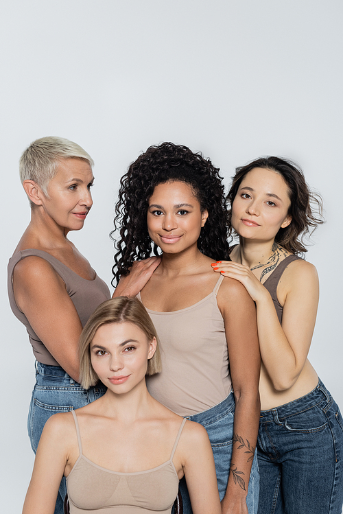 Women touching smiling african american friend isolated on grey, feminism concept