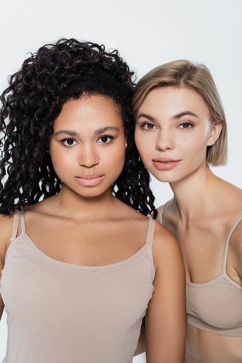 Blonde and african american women looking at camera isolated on grey