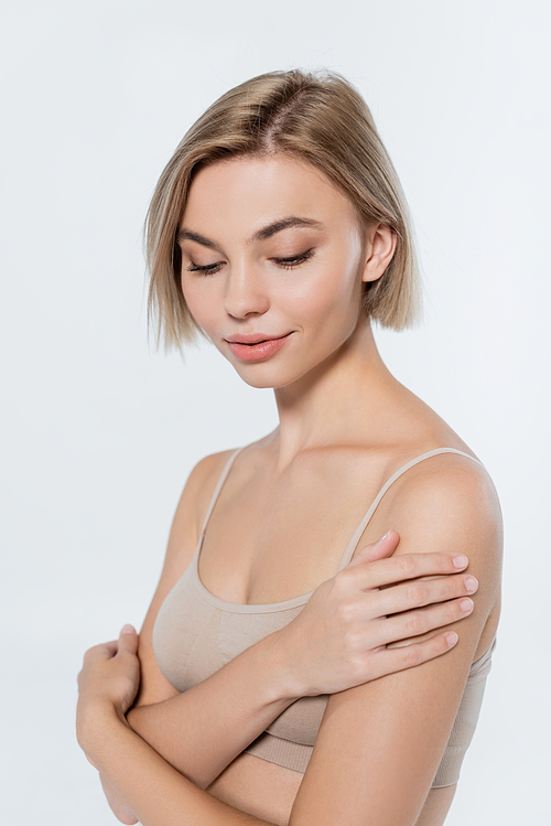 Young blonde woman touching shoulder isolated on grey