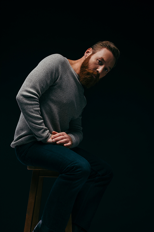 Trendy man in jumper posing on chair isolated on black with shadow