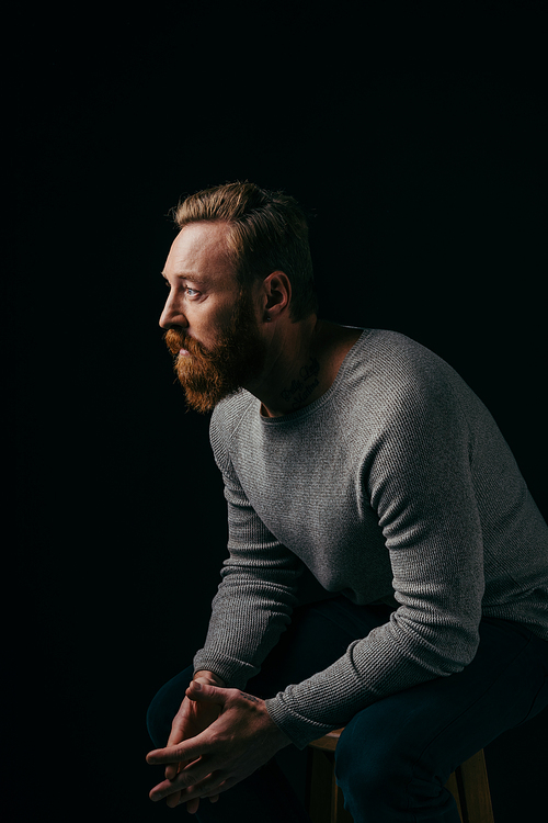 Bearded man in grey jumper looking away isolated on black with shadow