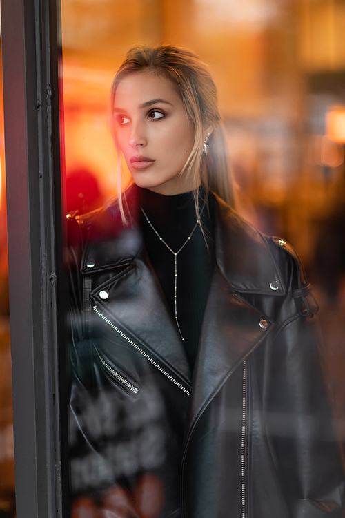 blonde woman in black leather jacket looking through glass window in New York