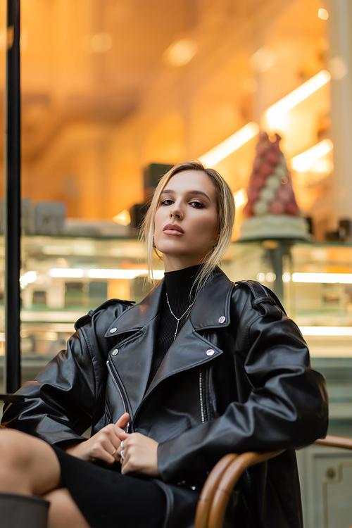 young blonde woman in black leather jacket sitting near outdoor cafe in New York