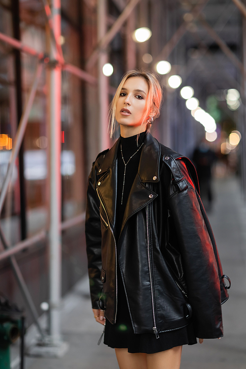 blonde woman in black leather jacket standing on street in New York city at evening time