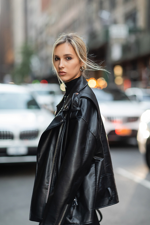 portrait of blonde woman in stylish leather jacket looking at camera on urban street in New York