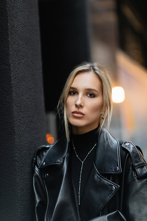 portrait of blonde woman in black leather jacket looking at camera outside