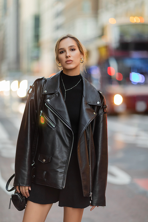 woman in stylish black outfit standing near blurred cars on street in New York city