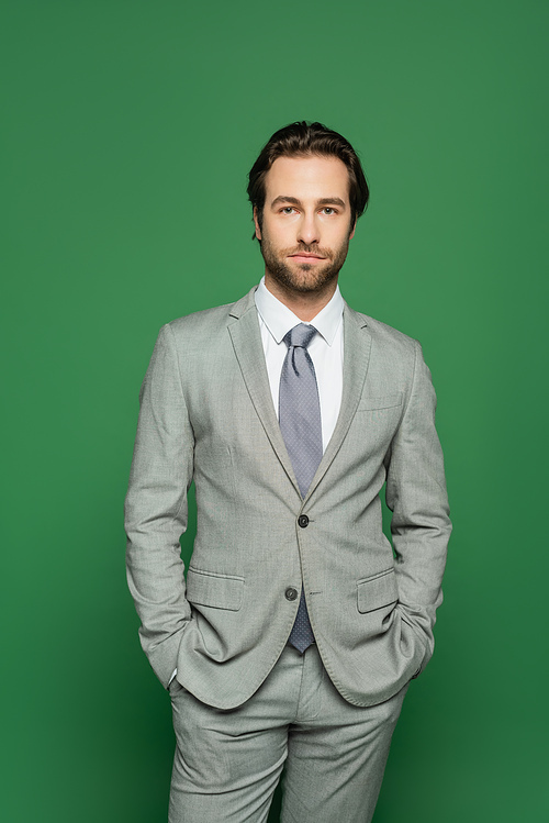 Brunette newscaster in suit holding hands in pockets isolated on green