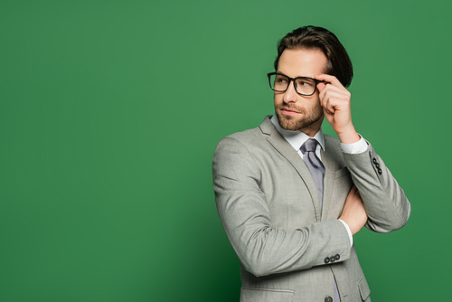 Young newscaster in suit touching eyeglasses on green background