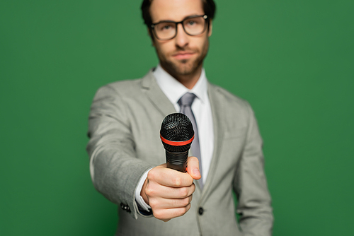 Blurred newscaster in suit holding microphone isolated on green