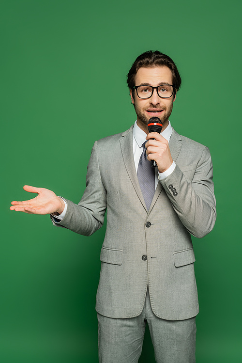 news anchor in suit talking at microphone and pointing with hand on green background