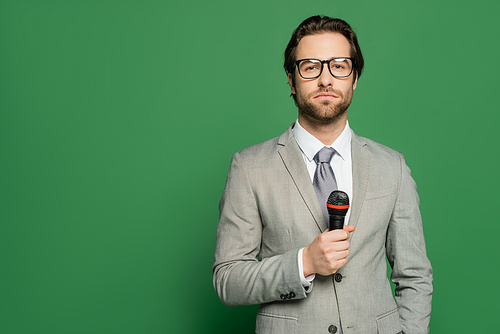 Brunette newscaster in eyeglasses holding microphone and looking at camera on green background