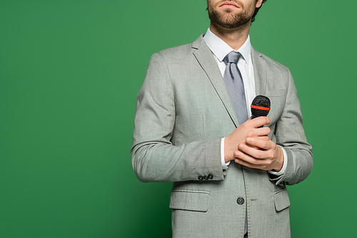 Cropped view of newscaster holding microphone on green background