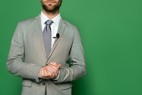 Cropped view of news presenter in suit and clip microphone standing on green background