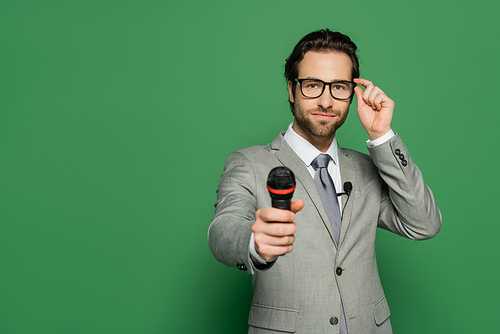 news anchor in suit adjusting eyeglasses while holding microphone on green background