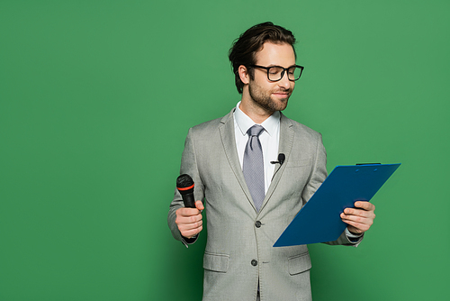 broadcaster in suit and eyeglasses holding clipboard and microphone on green