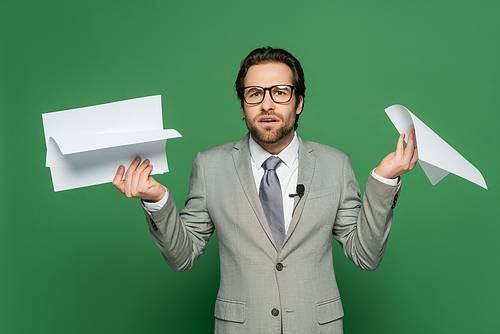 confused news anchor in eyeglasses and suit holding blank papers on green