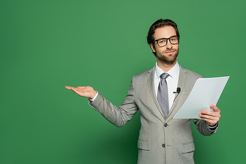 news anchor in eyeglasses and suit holding blank paper and pointing with hand on green