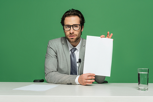 bearded news anchor in eyeglasses and suit holding blank paper isolated on green