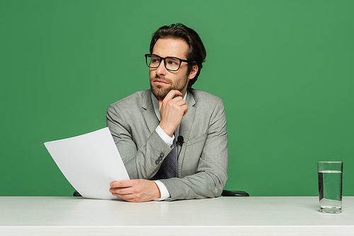 thoughtful broadcaster in eyeglasses and suit holding blank paper isolated on green