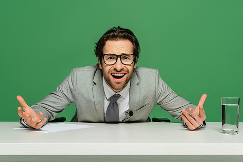 emotional news anchor in eyeglasses and suit gesturing isolated on green