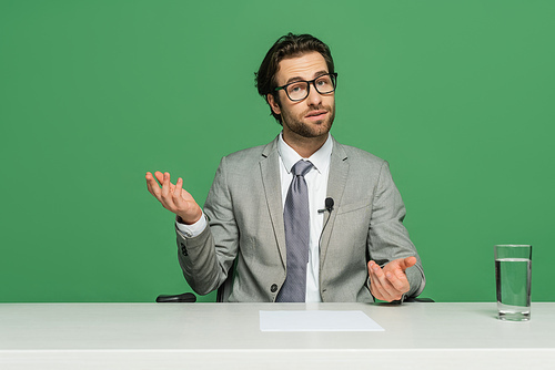 news broadcaster in eyeglasses and suit sitting at desk and talking isolated on green