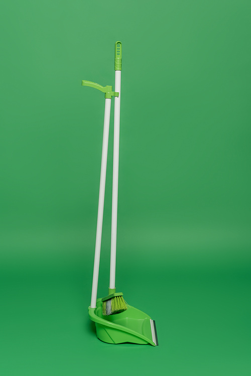 broom and plastic scoop on green background, housekeeping concept