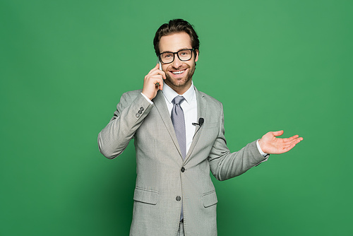 smiling reporter in eyeglasses and suit talking on smartphone on green background