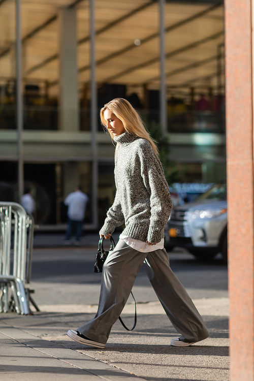 full length of stylish young woman with blonde hair walking in trendy winter outfit in New York