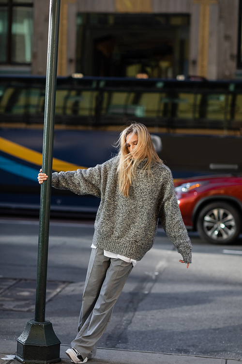 full length of stylish young woman in grey winter outfit posing near street pole in New York city
