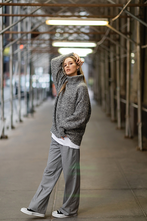 full length of stylish young woman in trendy winter outfit posing on urban street in New York