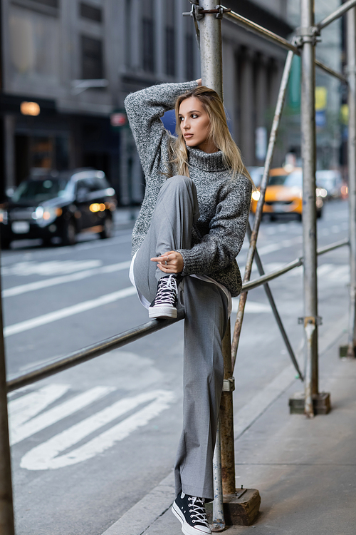 full length of stylish young woman in trendy winter outfit sitting on urban street in New York