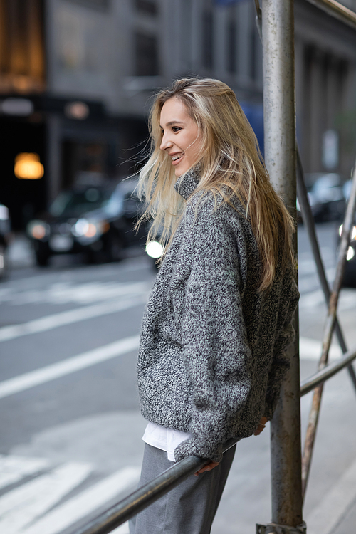 cheerful woman in grey knitted sweater smiling on urban street in New York city