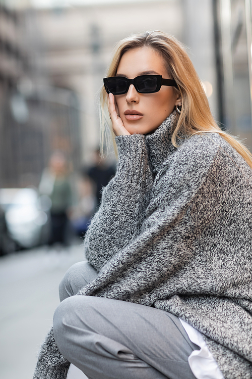 blonde woman in grey winter sweater and trendy sunglasses sitting on urban street in New York city