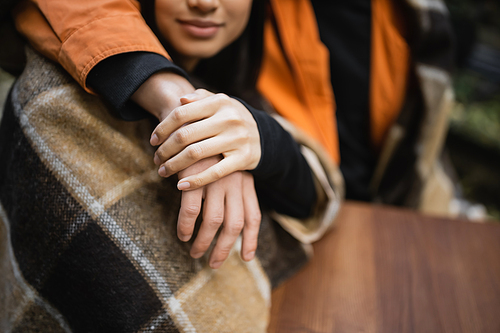 Cropped view of woman in blanket holding hand of boyfriend in outdoor cafe