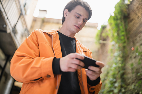 Low angle view of young man using cellphone on terrace of cafe